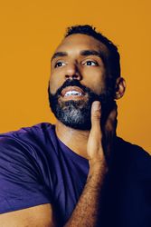 Black man in yellow studio with one hand to his face