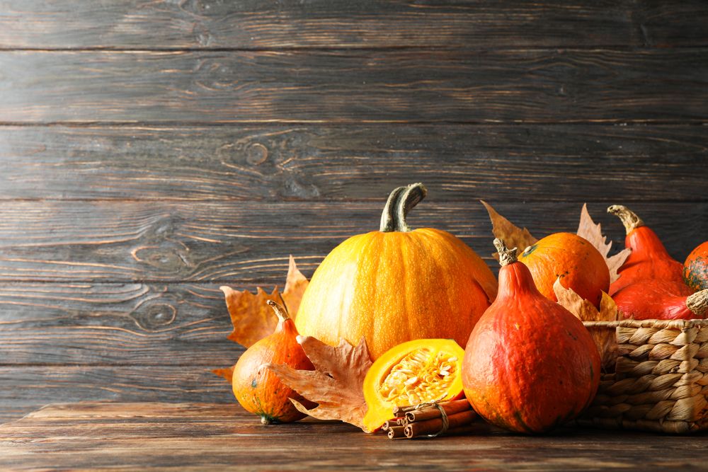 Straw basket, pumpkins, leaves and cinnamon on wooden background, copy space