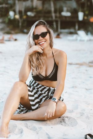 Woman in dark bikini top sitting on sand