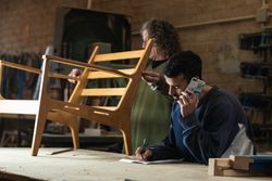 Focused man talking on smartphone and writing notes in carpentry