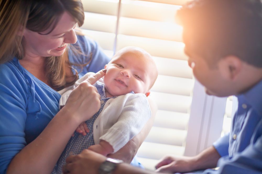 Happy Couple Enjoying Their Newborn Son In The Light of The Window.