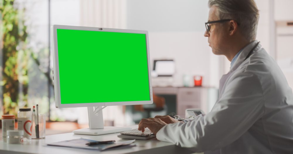 Healthcare Doctor Working on Desktop Computer with Green Screen Mock Up Display.