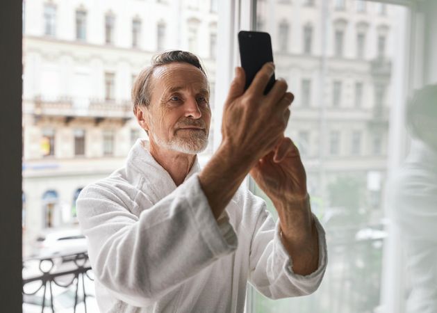 Grey haired man with beard taking a selfie out the hotel window