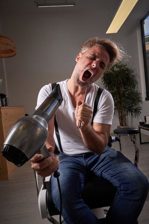 Funny man singing in hairbrush and hair dryer
