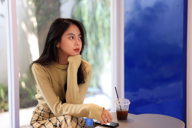 Asian Teenager Sitting at Cozy Cafe with A Cup of Americano