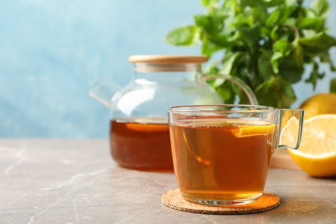 Cup of tea, lemon, teapot and mint on grey background, close up