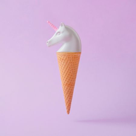 Painted unicorn head in ice cream cone on pastel purple background