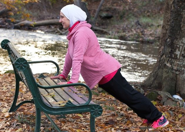 Woman wearing hijab doing push-ups on wooden bench in park