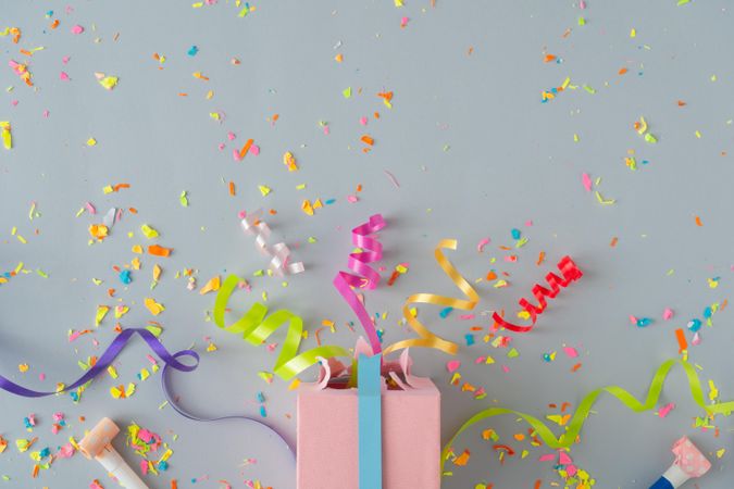 Present with confetti and colorful streamings on grey background