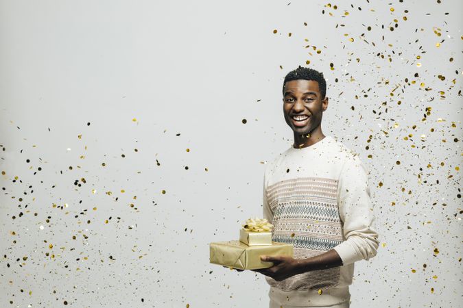 Smiling Black man holding two presents wrapped in gold paper with glitter falling