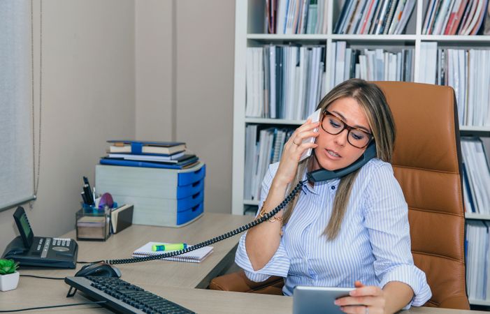 Busy businesswoman talking between two phones in office