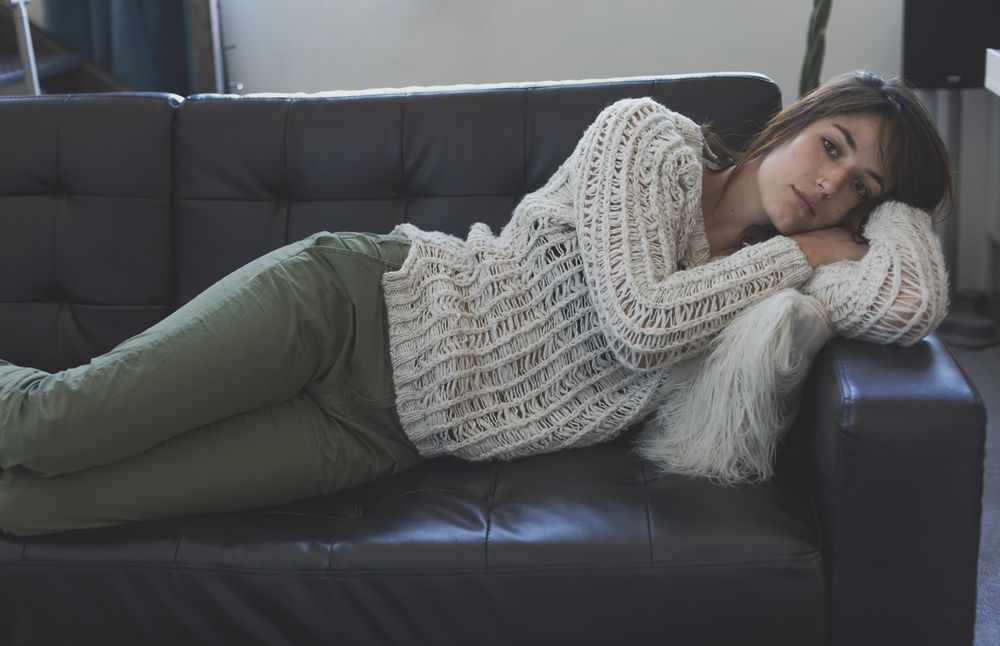 Female in wooly sweater lying on her side trying to nap on leather couch in living room