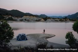 Man and dog looking over lake with tent at dusk 4MOJa0