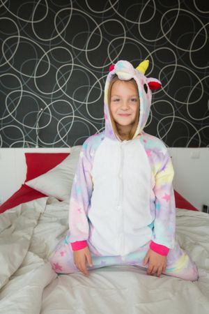 Cheerful girl in unicorn pajama having fun on bed