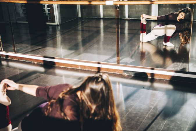 Young ballet dancer warming up body and stretching in front of mirror.