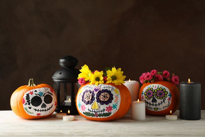 Pumpkins with catrina skull makeup and halloween accessories on brown background