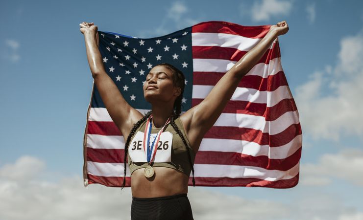 Female athlete with medal holding American flag with her eyes closed