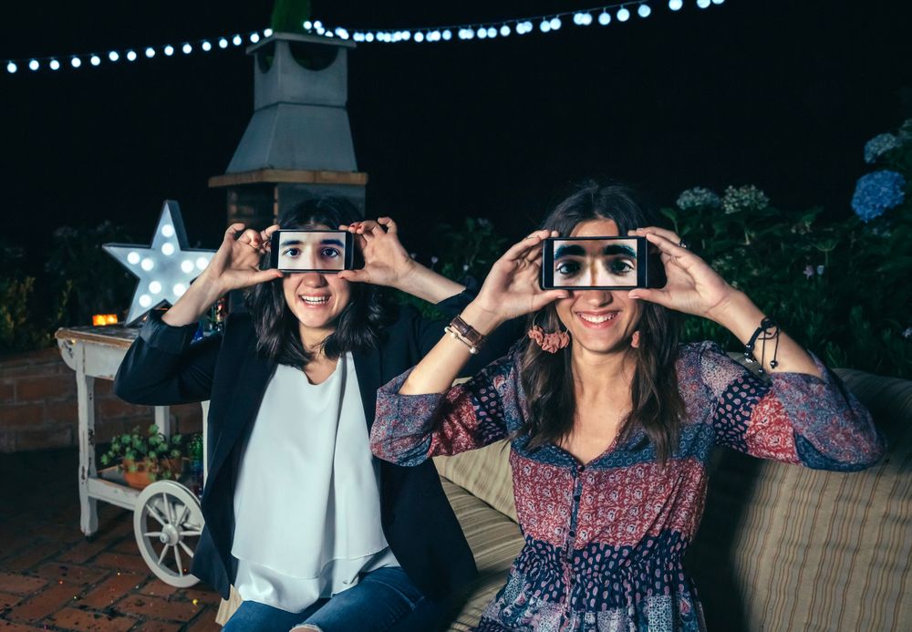 Funny women holding smartphones showing male eyes