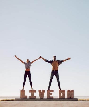 Man and woman having a great time together standing on block letters that spell “live on”