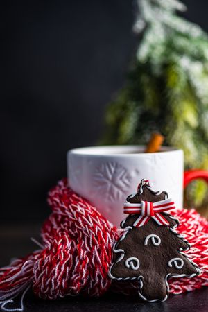 Side view of cup of mulled tea wrapped in cosy scarf with tree shaped cookie