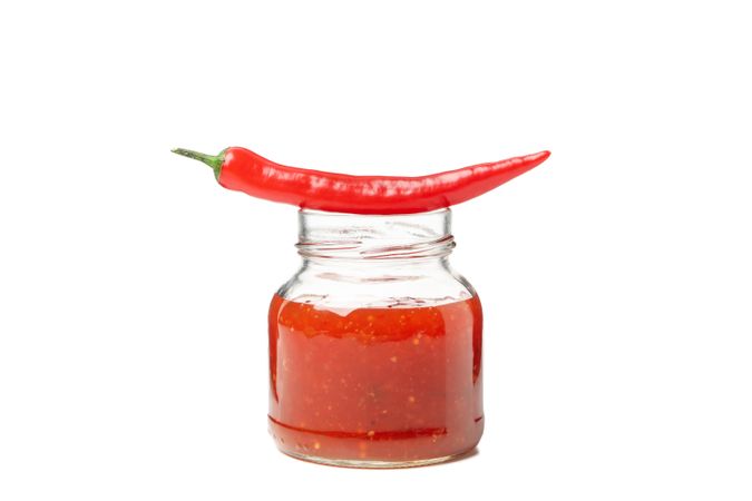 Chilli pepper and glass jar of sauce isolated on plain background