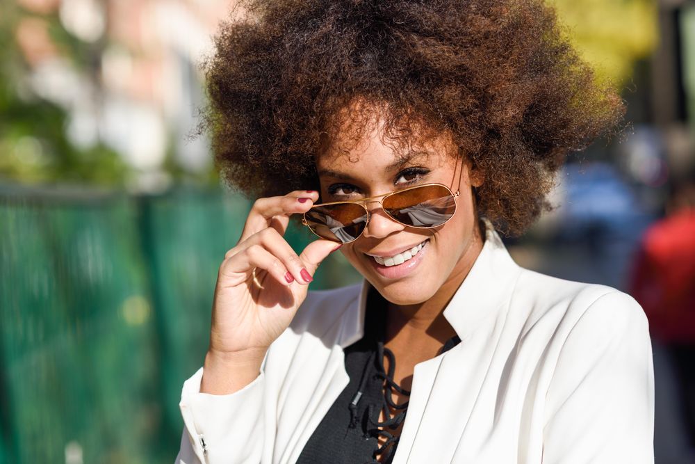 Smiling stylish female looking up from aviators sunglasses on street