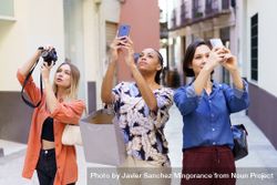 Three women looking up and taking pictures with their phone in narrow lane 0vl2d4