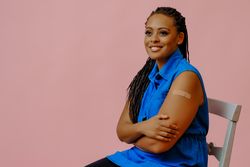 Smiling female sitting with bandage after immunization in pink studio shoot, copy space