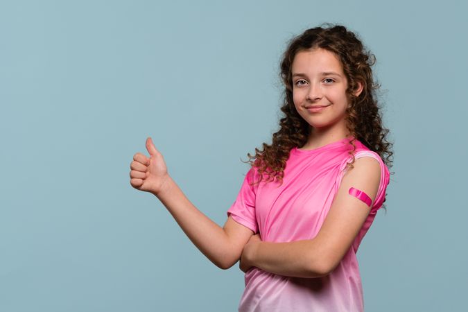 Smiling girl giving thumbs up after vaccination.