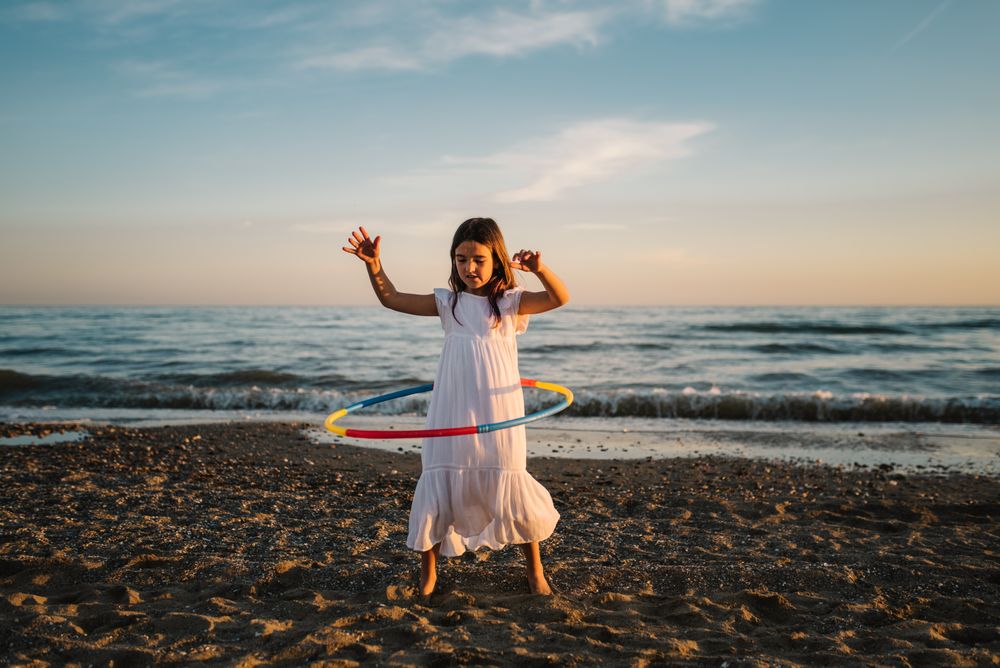 Adorable girl playing with hula hoop ribbon on seaside