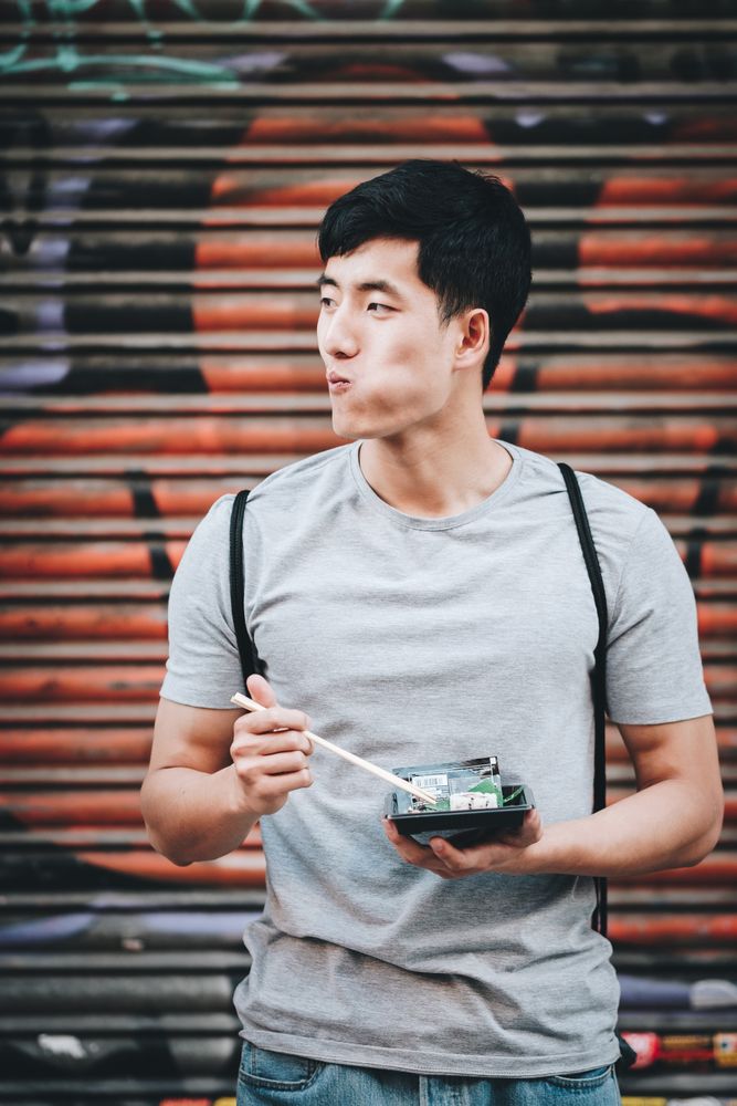 Asian man eating takeaway food with chopsticks on city street