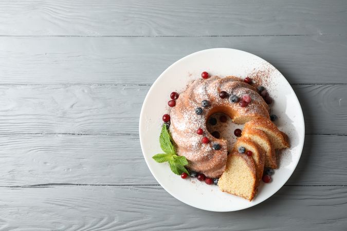 Cake with powdered sugar, berries and mint on wooden background, top view