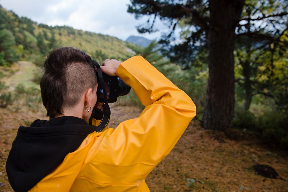 Enthusiastic person in yellow raincoat photographing tree in mountain