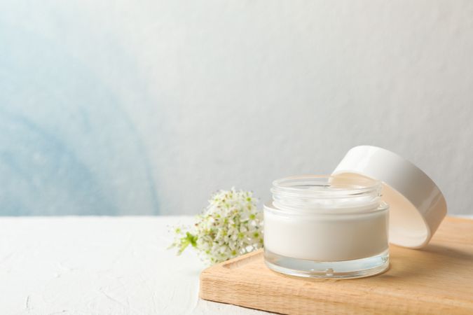 Jar with cream, allium flowers and board on neutral background, copy space
