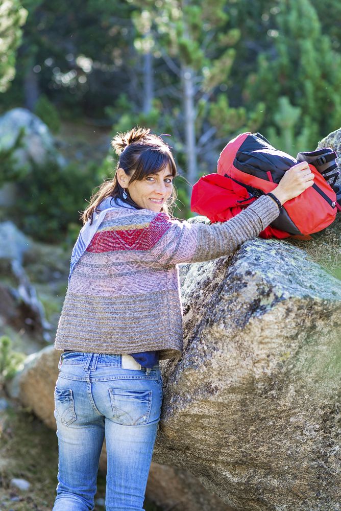 Brunette woman turning around while taking backpack down from rock in the woods