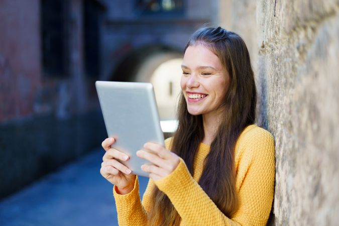 A cheerful young woman enjoys her tablet outdoors, embracing her surroundings and friends