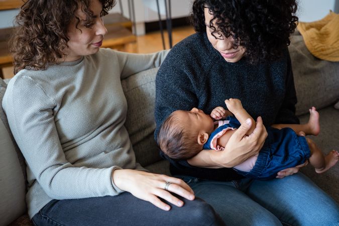 New family of two moms and a bay sitting close together on a couch