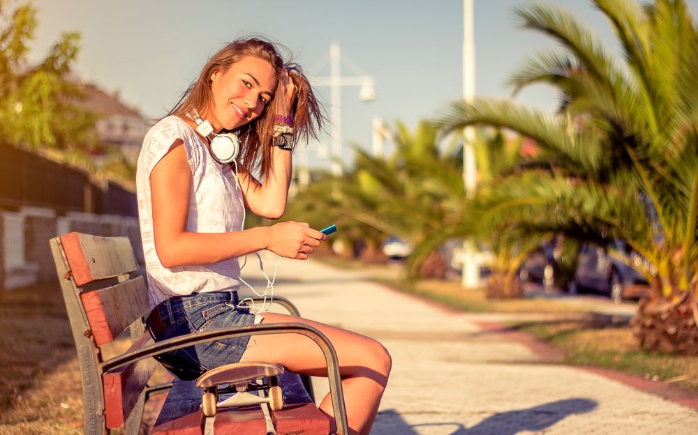 Young girl with skateboard and headphones looking smartphone