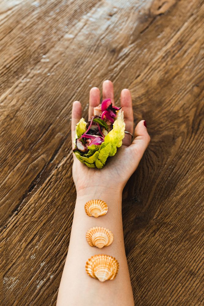 Crop female hand with lettuce wrap and seashells