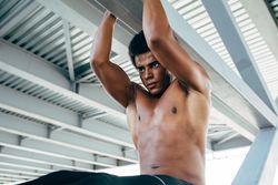 Athletic Black male doing pull ups on the underpass of a bridge