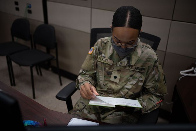 US female soldier with facemask reading book on her desk