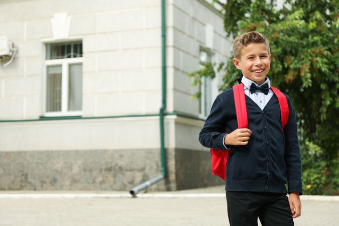 Boy with backpack against school building, space for text