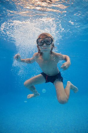 Carefree boy swimming underwater in pool with clear water