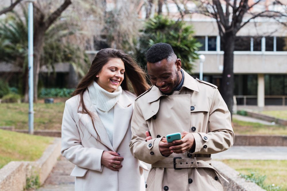 Joyful multiethnic couple using smartphone in park