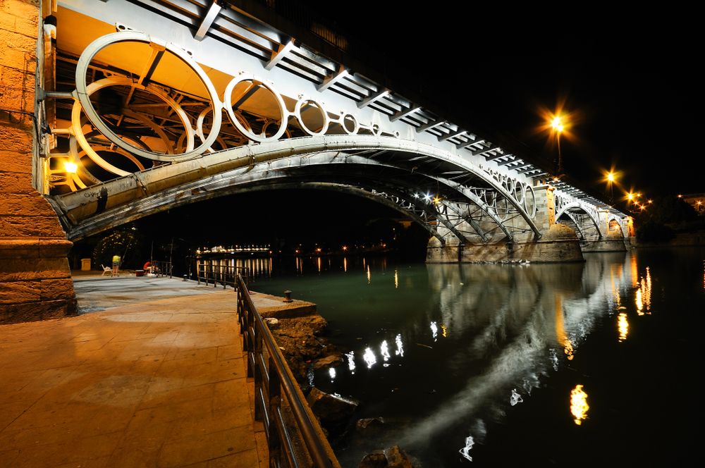 Under the Triana Bridge over Guadalquivir river at sunset with river reflections