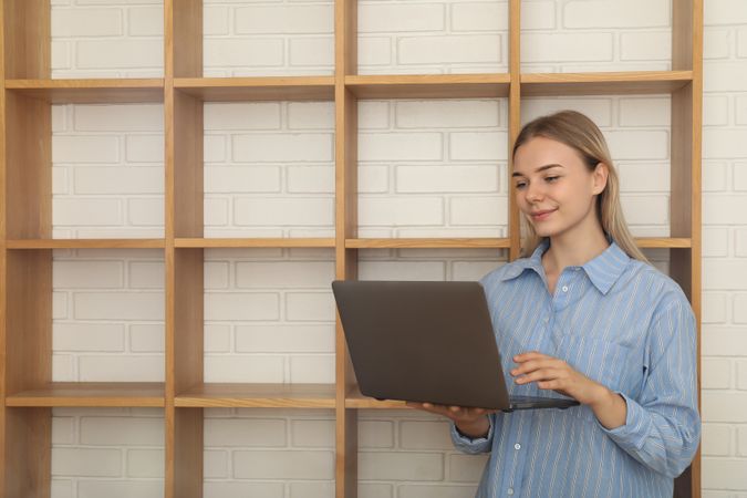 Young woman with laptop standing in modern flat, space for text