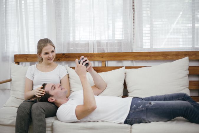 Man lies on woman’s lap as they both look at his phone