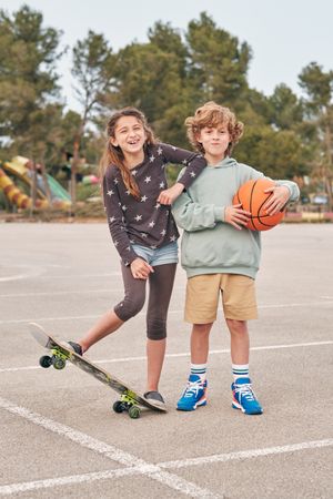 Happy teenagers with skateboard and basketball in city
