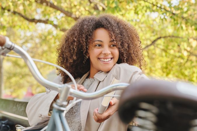 Smiling Black woman sitting on bench in park with book