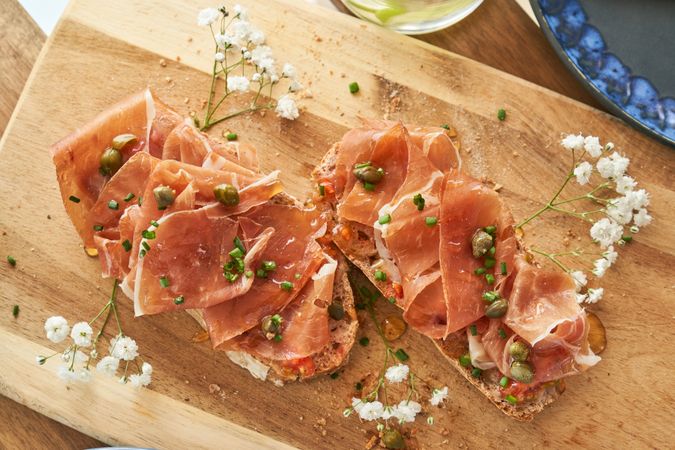 Appetizing prosciutto toasts with capers served on wooden board